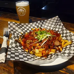 Pig & Duke Special: Pork Belly Poutine [Picture: Plated Pork Belly Poutine with Sea Change branded pint and napkin wrapped fork on wood table]